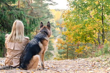 Naklejka na ściany i meble Back view of sitting woman and dog in autumn wood on the mountain