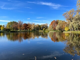 Autumn trees silhouettes reflection on the surface of the lake, blue sky