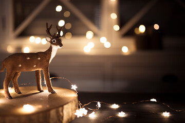 Miniature reindeer on wooden tray, with glowing string lights in the background. Christmas...