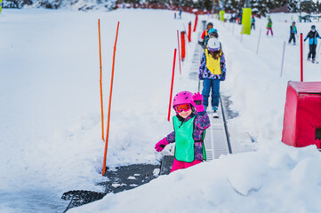 Young skier, girl waving and smiling while going up on ski conveyor. Ski winter holidays in Andorra, El Tarter, Pyrenees Mountains, Grandvalira - obrazy, fototapety, plakaty