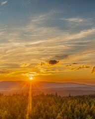 A panoramic view of a serene sunset in the rugged mountains, seen from a high vantage point. The...