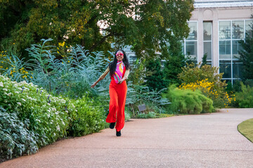 an African American woman wearing an orange jumpsuit skipping along a footpath the garden surrounded by colorful flowers and lush green trees at Atlanta Botanical Garden in Atlanta Georgia USA