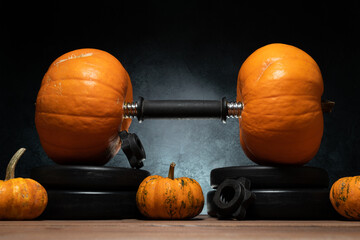 Dumbbell barbell with two orange pumpkins as a weight plates. Gym weightlifting workout and sport training concept. Healthy fitness lifestyle autumn or fall composition for Halloween or Thanksgiving.