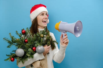 Smiling young female 20s wears cozy white sweater and Christmas hat holding bouquet of spruce...