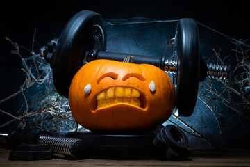 Carved Halloween pumpkin lifting a heavy barbell dumbbell. Weightlifting carving idea with...