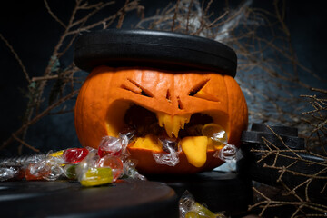 Dumbbell barbell weight plates crushing carved Halloween pumpkin Jack-o'-lantern head. Candy spills...