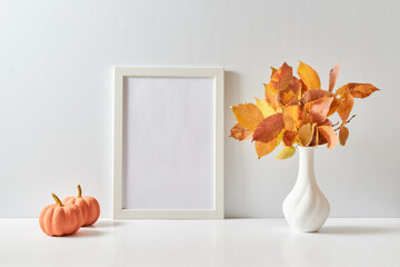Mockup with a white frame and colorful autumn leaves in a vase on a light background. Empty poster...