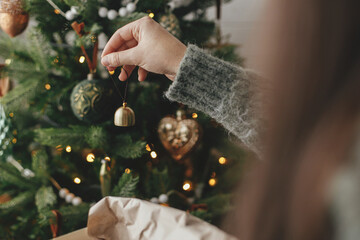 Hands decorating christmas tree with stylish bauble in atmospheric festive room. Merry Christmas!...