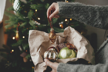 Hands decorating christmas tree with stylish bauble in atmospheric festive room. Merry Christmas!...