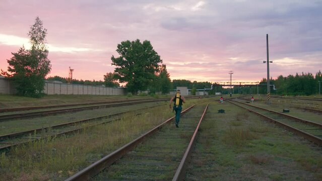 Young muscular man training with a balloon drager on his back and running between the rails at sunset. Back view