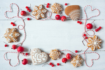 Christmas white wooden background with gingerbread snowflakes, heart, rope, red apples and berries, space for greeting text, top view.