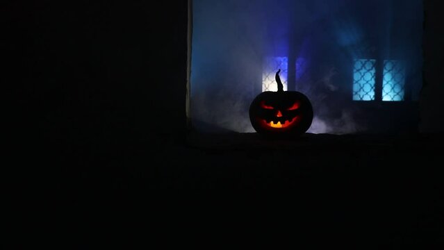 Scary Halloween pumpkin in the mystical house window at night or halloween pumpkin in night on abandoned room with window. Selective focus