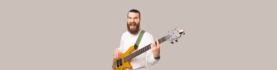 Banner shot of a screaming young bearded man playing his bass wooden guitar.