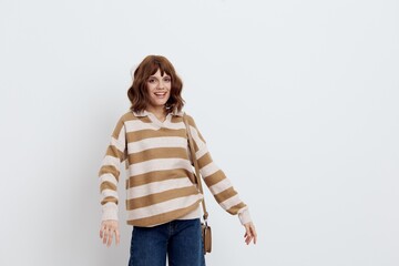 an emotional woman stands on a white background in a striped sweater and a bag on her shoulder ,...