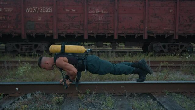 Young muscular man with a drieger balloon on his back is training at the railroad station and doing push-ups on one rail