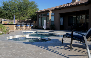 A desert landscaped backyard in Arizona featuring a travertine tiled pool deck with spa and outdoor...