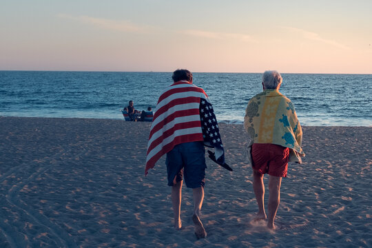 Couple walking on the beach during sunset with the American flag on their backs - Powered by Adobe