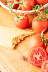 Pasta, beautiful details of red tomatoes and strands of raw spaghetti over rustic wood, selective focus.