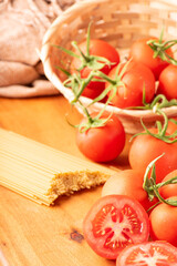 Pasta, beautiful details of red tomatoes and strands of raw spaghetti over rustic wood, selective focus.