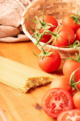 Pasta, beautiful details of red tomatoes and strands of raw spaghetti over rustic wood, selective focus.