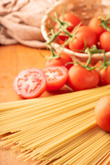 Pasta, beautiful details of red tomatoes and strands of raw spaghetti over rustic wood, selective focus.