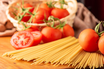 Pasta, beautiful details of red tomatoes and strands of raw spaghetti over rustic wood, selective focus.