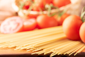 Pasta, beautiful details of red tomatoes and strands of raw spaghetti over rustic wood, selective focus.