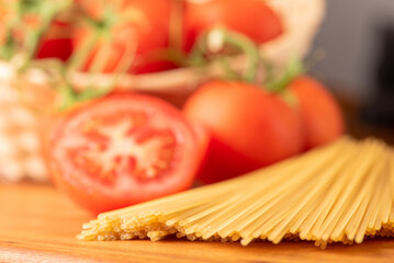 Pasta, beautiful details of red tomatoes and strands of raw spaghetti over rustic wood, selective focus.