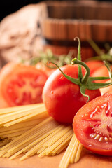 Pasta, beautiful details of red tomatoes and strands of raw spaghetti over rustic wood, selective focus.