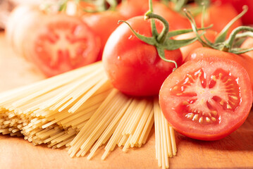 Pasta, beautiful details of red tomatoes and strands of raw spaghetti over rustic wood, selective focus.