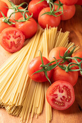 Pasta, beautiful details of red tomatoes and strands of raw spaghetti over rustic wood, top view.