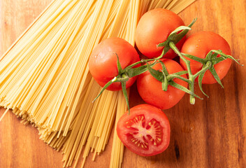 Pasta, beautiful details of red tomatoes and strands of raw spaghetti over rustic wood, top view.