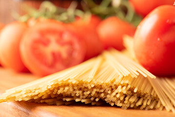 Pasta, beautiful details of red tomatoes and strands of raw spaghetti over rustic wood, selective...