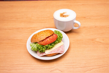 Ham sandwich with cheese, tomato, and lettuce and a cup of coffee.