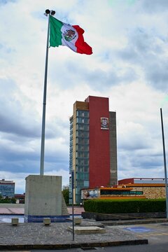 Vertical shot of the campus of the UNAM university with a modern red building and the Mexican flag