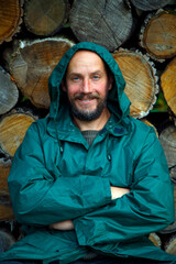 Portrait of a bearded man on a background of firewood. A bearded man poses for the camera after cutting firewood in the forest. The concept of masculinity, naturalism, survival.