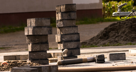 Układanie kostki na placu przed domem . Brukowanie podjazdu , widoczna kostka brukowa w stosikach  oraz łopata , szpachelka i młotki gumowe ponadto poziomica i przyczepka samochodowa . © Grzegorz