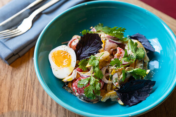 salad with onion, egg, sweet pepper, herbs on a plate in a restaurant on the table