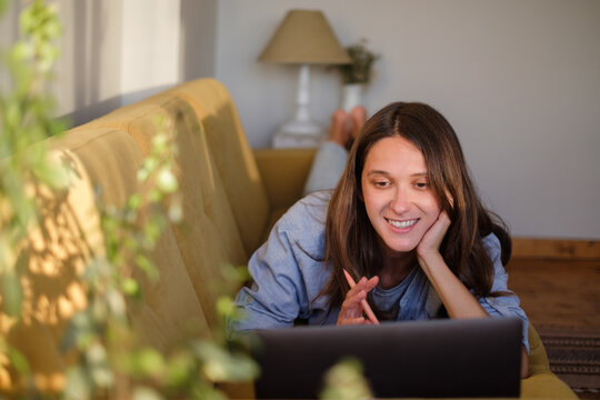 Woman with laptop and notebook lying on the sofa at home