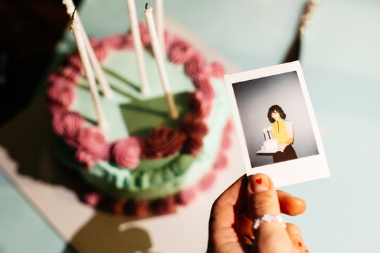 Curly girl showing a polaroid photo and a cake on her birthday party 