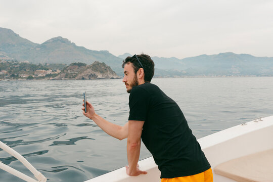 Young man aboard small vessel taking picture  on smartphone