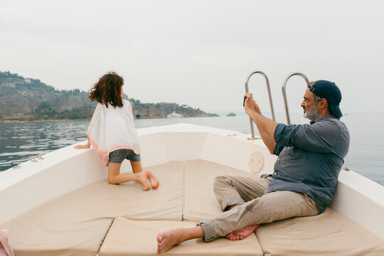 Man taking a photo with smartphone of his daughter aboard a small boat