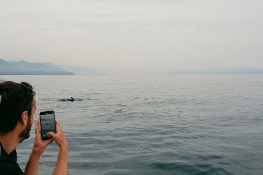 Young man taking picture of dolphin in the sea with smartphone
