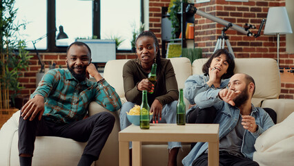 Diverse people having fun watching movie together, enjoying action film on tv channel program. Laughing at funny television series or show, drinking beer at chill hangout. Tripod shot.