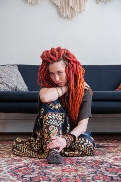 Female hippie sitting on ornamental carpet near sofa