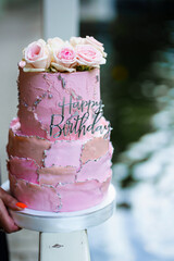 Beautiful two-tier pink cake with rosebuds and the inscription happy birthday. 