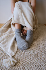 The woman lies in warm gray socks in bed and covers herself with a blanket. Women's legs in cozy...