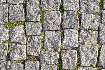 Stone road paved with asymmetrical stones with sprouted grass at seams. Textured background, top view
