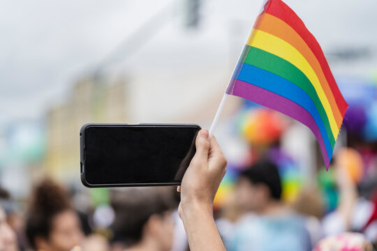 unrecognizable person filming with cell phone and lgbt flag