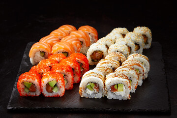 Different types of delicious and juicy sushi and rolls on a black board